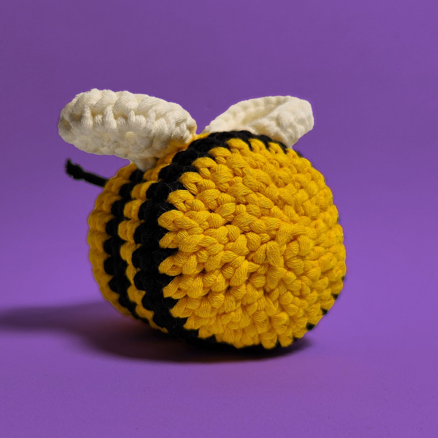 Yellow smiling bee with black stripes, and white wings crochet amigurumi, a completed project from our beginner-friendly crochet kit. Handmade with our yarn, perfect for people who are looking to learn crocheting. Back view.