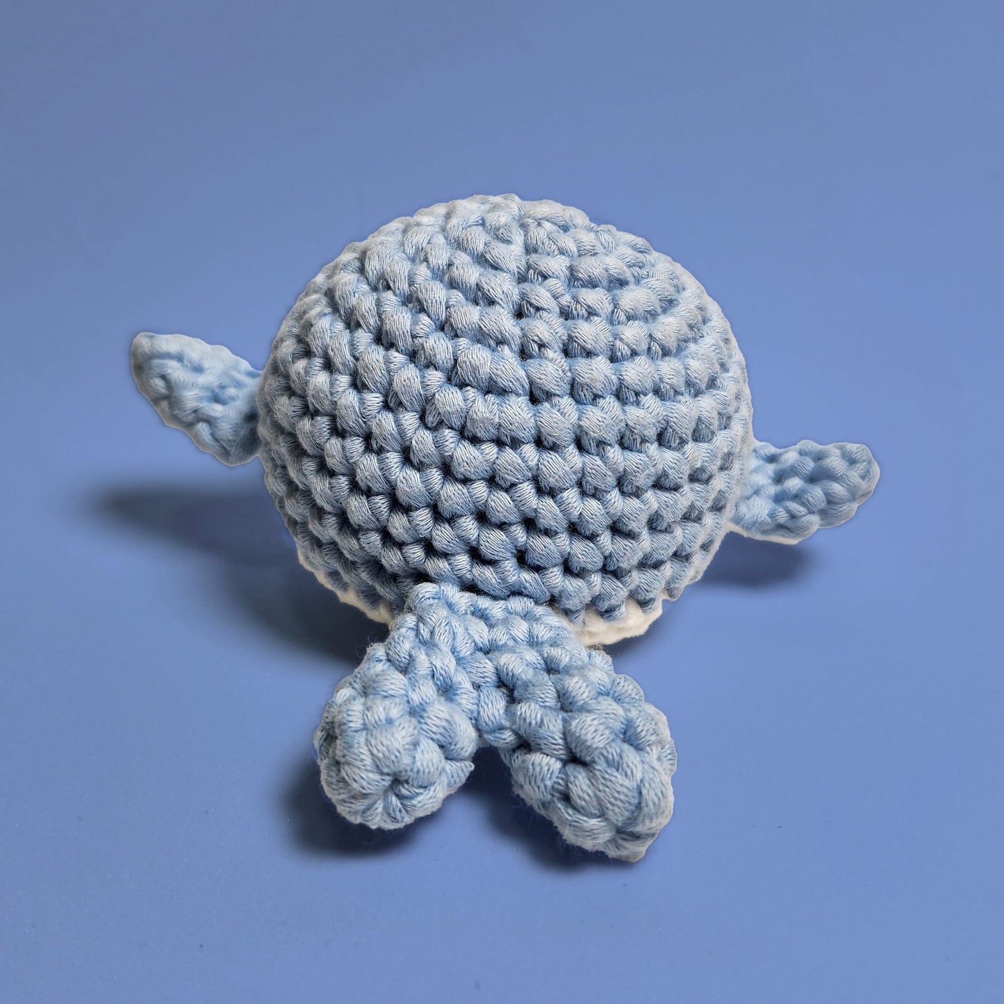 Blue and white amigurumi whale, handcrafted with care. Made from our beginner-friendly crochet kit, perfect for those new to crocheting. Back view showing the heart-shaped tail.