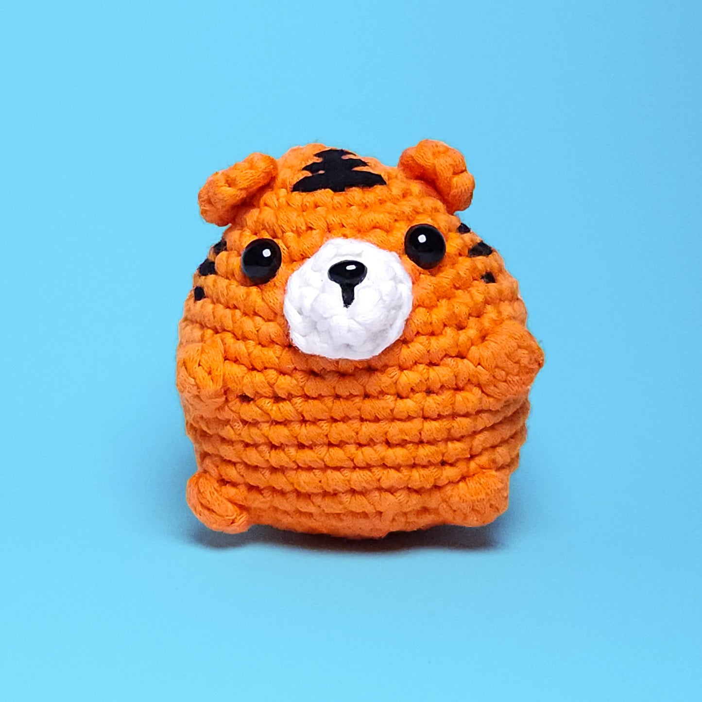 Cute chubby orange tiger amigurumi with black stripes, made from our beginner-friendly crochet kit. Perfect for those new to crocheting, showcasing its adorable and detailed design. Front view.