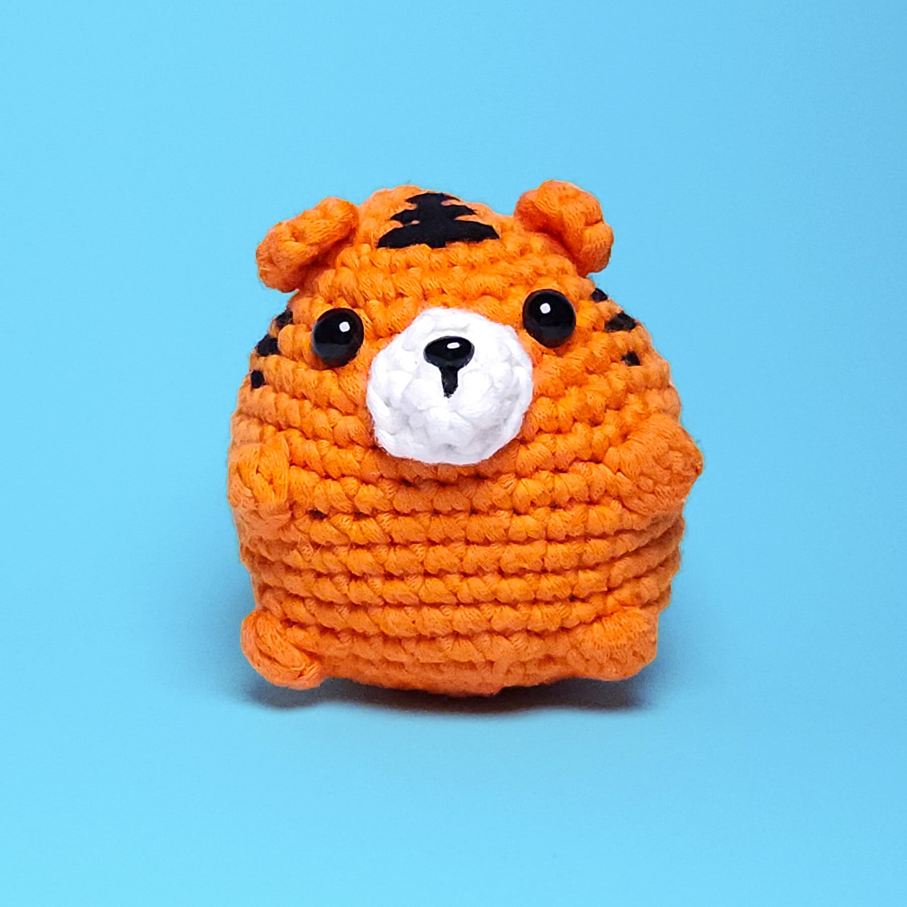 Cute chubby orange tiger amigurumi with black stripes, made from our beginner-friendly crochet kit. Perfect for those new to crocheting, showcasing its adorable and detailed design. Front view.