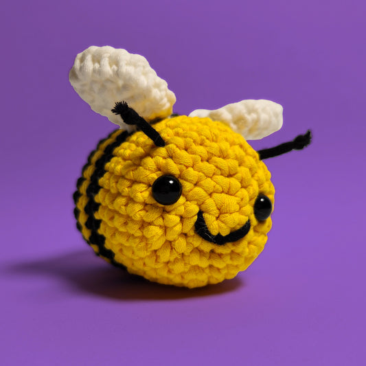Yellow smiling bee with black stripes, and white wings crochet amigurumi, a completed project from our beginner-friendly crochet kit. Handmade with our yarn, perfect for people who are looking to learn crocheting. Front view.