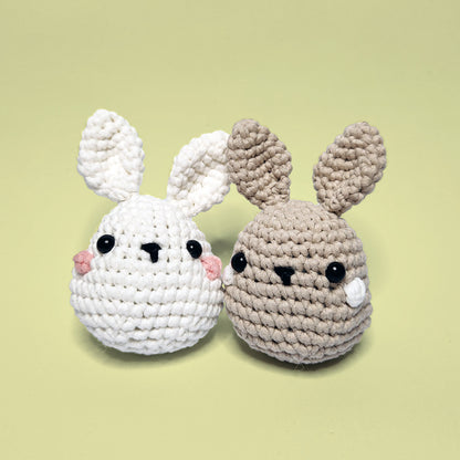 Two adorable crochet bunnies, one brown and white, side by side. Made using our beginner-friendly crochet kits.