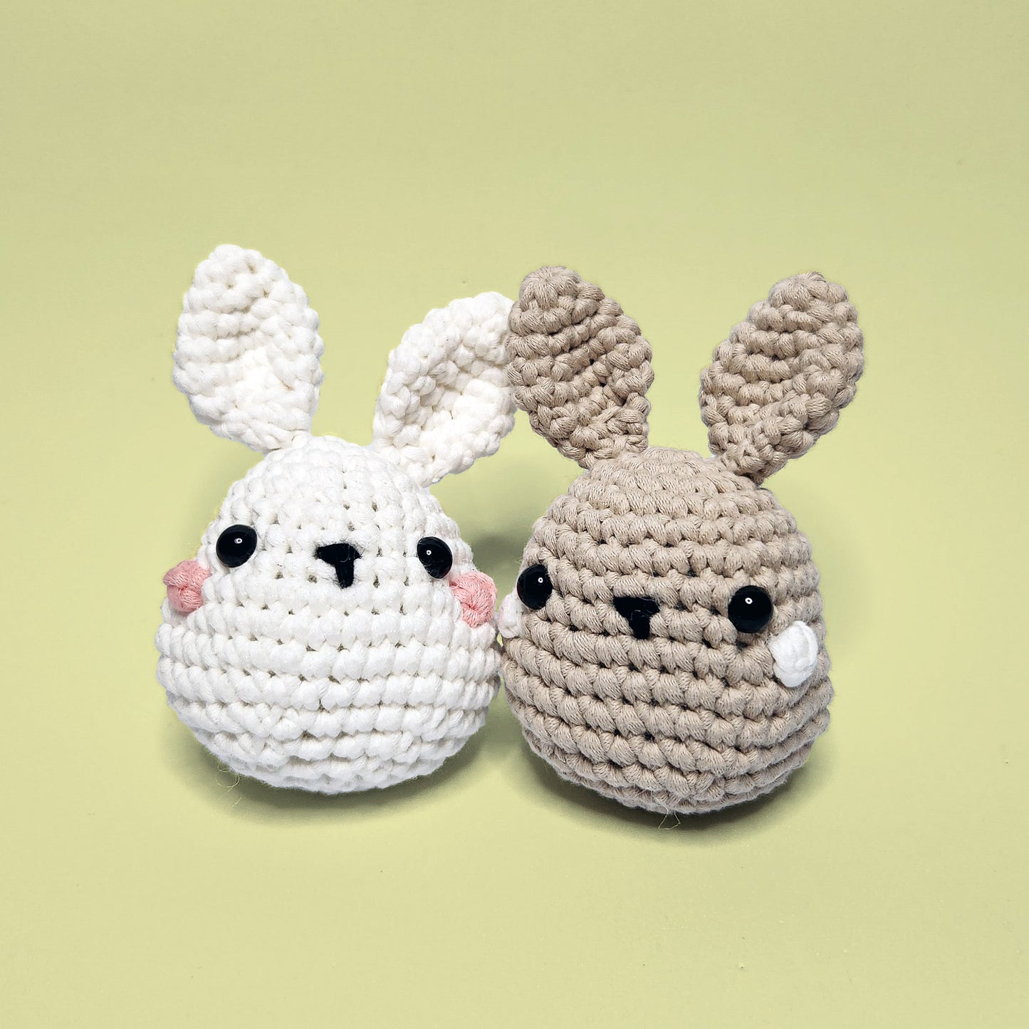 Two adorable crochet bunnies, one brown and white, side by side. These are completed projects from our beginner-friendly crochet kit. Handmade with our yarn, perfect for people who are looking to learn crocheting.