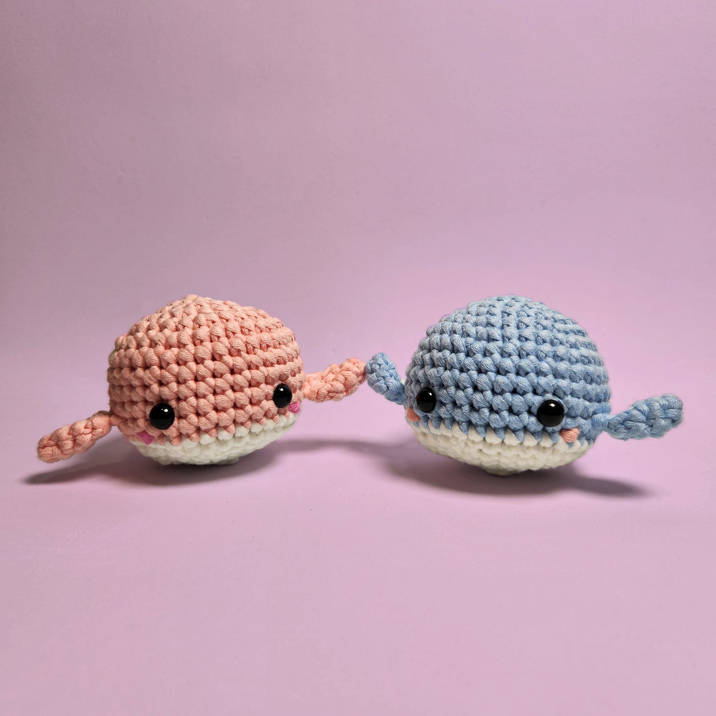 Pair of adorable amigurumi whales, one blue and one pink, with blush accents. Handcrafted with care and perfect for those new to crocheting using The Squishy Pals crochet kits.