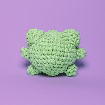 Cute green amigurumi frog, handcrafted from our beginner-friendly crochet kit. Ideal for beginners learning to crochet. Back view.