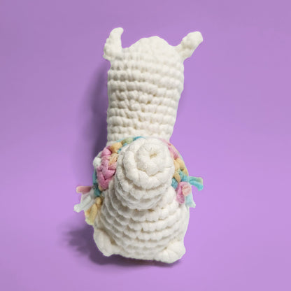 White alpaca crochet amigurumi with a rainbow yarn saddle, made from our beginner-friendly crochet kit. Handcrafted with love, this adorable alpaca is perfect for beginners and alpaca enthusiasts. Back view showcasing its charming design and colorful saddle.