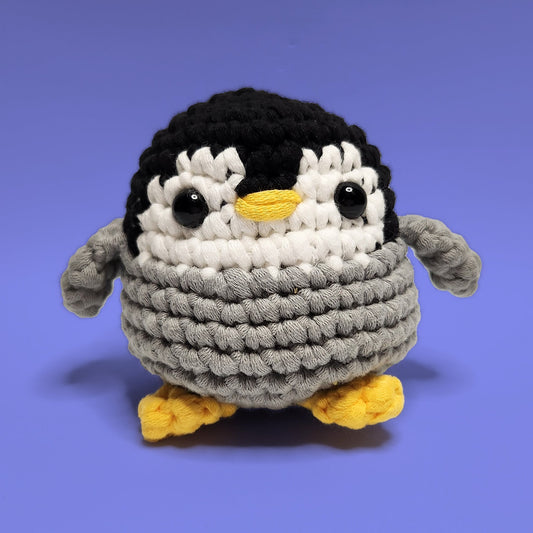Lola the black, grey and white penguin crochet amigurumi, handmade with love. This adorable penguin with yellow legs is perfect for bringing joy and cheer. Front view, ideal for crochet enthusiasts and penguin lovers.