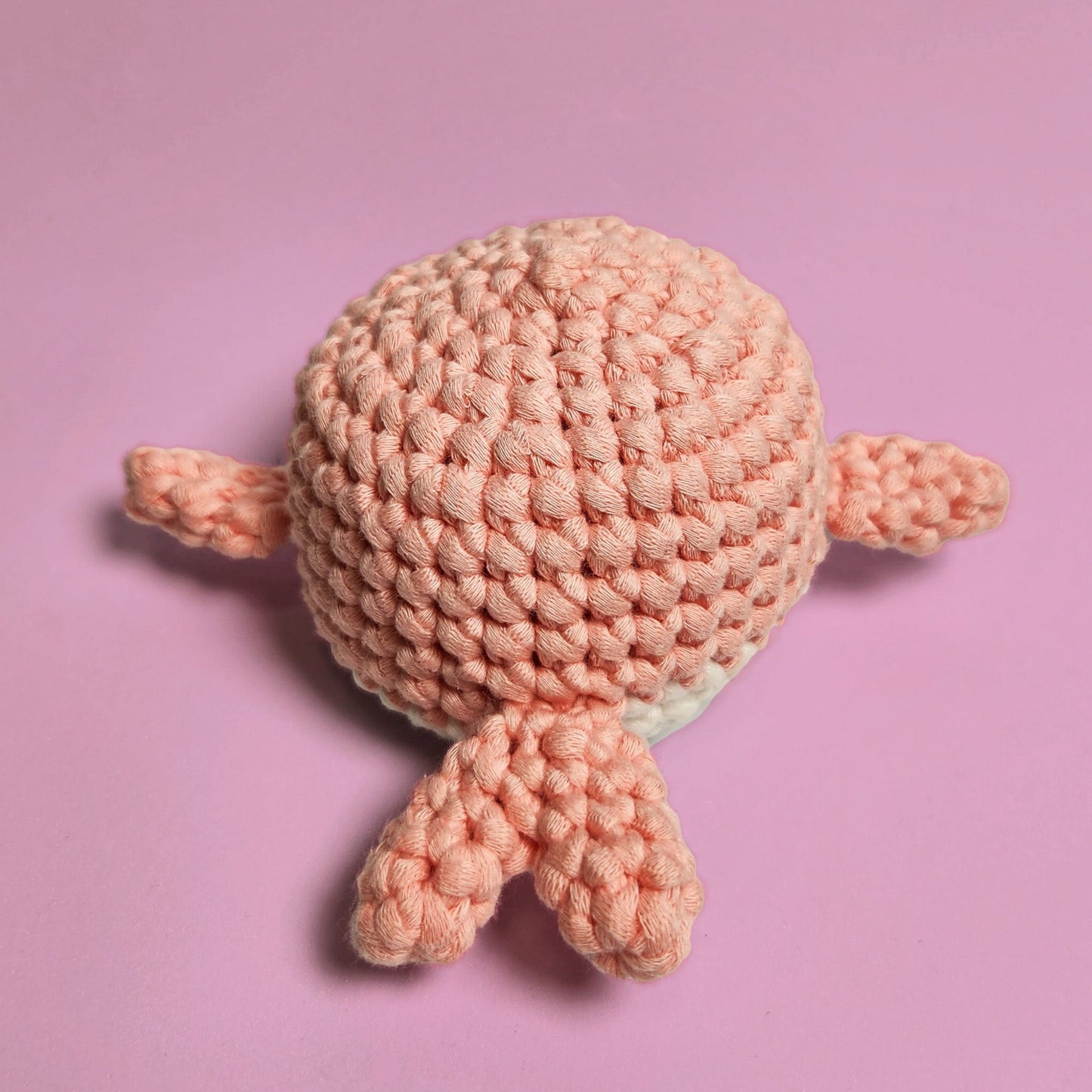 Pink and white amigurumi whale, handcrafted with care and attention to detail. Made from our beginner-friendly crochet kit, perfect for those new to crocheting. Back view.