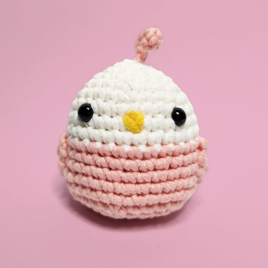 Pink and white lovebird crochet amigurumi with a cute feather accent. Handcrafted from our beginner-friendly crochet kit, ideal for those eager to learn crocheting. Front view.