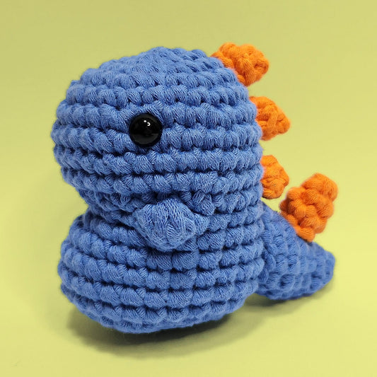 Blue dinosaur crochet amigurumi with a bulging stomach and orange spikes on the back. Handcrafted from our beginner friendly kit, this unique dinosaur is a fun and engaging project for crochet enthusiasts. Front view.