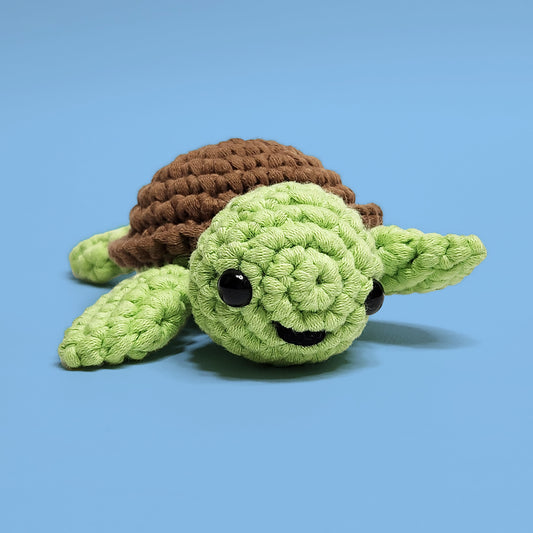 Green smiley turtle crochet amigurumi with a brown shell, made using our own beginner-friendly crochet kit. Handcrafted with love, this cheerful turtle is a delightful addition to any collection. Front view.