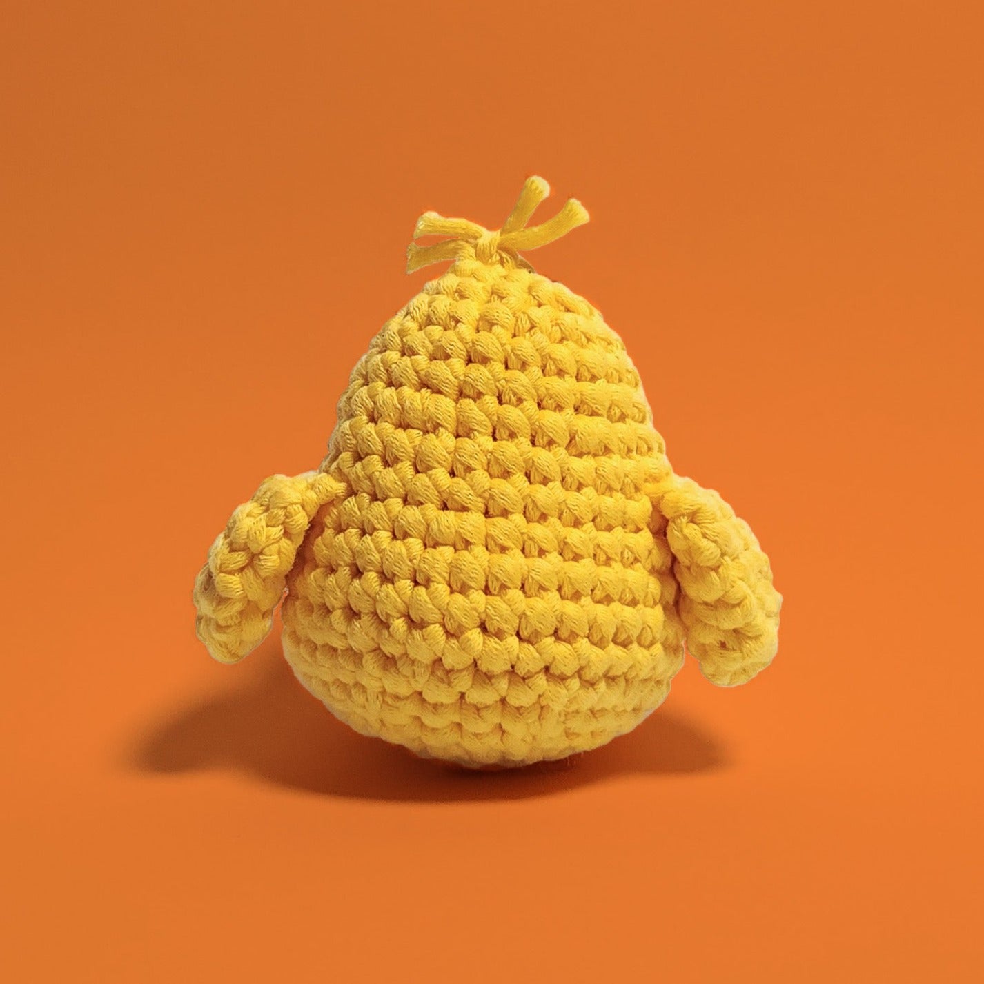 Yellow baby chick crochet amigurumi with adorable hair accents. Handcrafted with love using our beginner-friendly crochet kit, this charming chick is a delightful project for crafters of all levels. Back view.