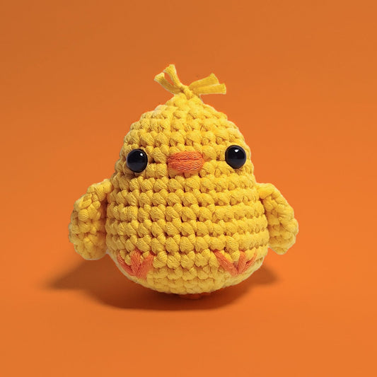 Yellow baby chick crochet amigurumi with adorable hair accents. Handcrafted with love using our beginner-friendly crochet kit, this charming chick is a delightful project for crafters of all levels. Front view.